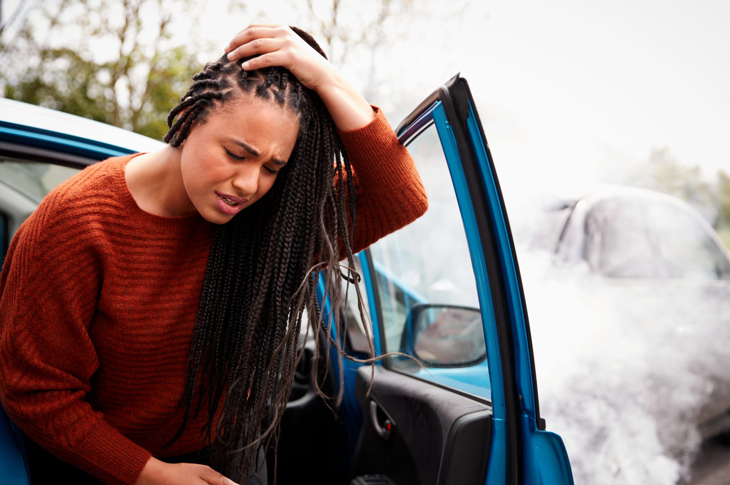 Depositphotos_299190602_XL - Warshafsky Law Firm Milwaukee, Wisconsin - Warshafsky Law Firm Milwaukee, Wisconsin Woman with braids and an orange sweater gripping her head beside an open blue car door, looking distressed or worried. Warshafsky Law Firm Milwaukee, Wisconsin Warshafsky Law Firm Milwaukee, Wisconsin